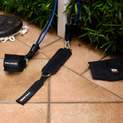 Fitness equipment, including the A90 Leg Day Set, laid out on a tiled floor next to a green plant, ready for an outdoor workout session.